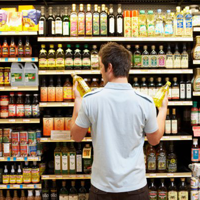 Man Choosing Between Two Olive Oils at Aisle In Store